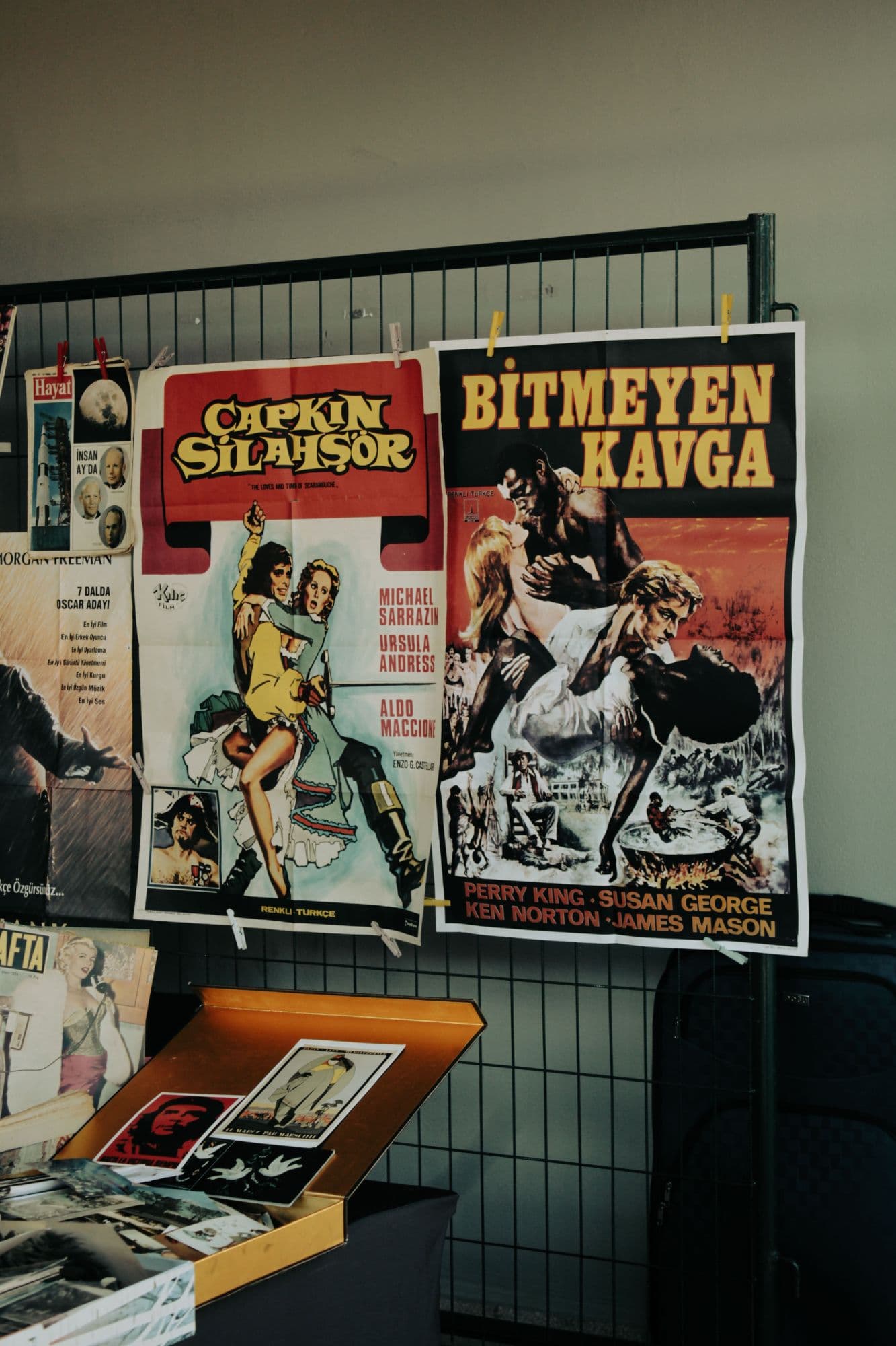 Vintage film posters pegged to a metal grid above a box of postcards